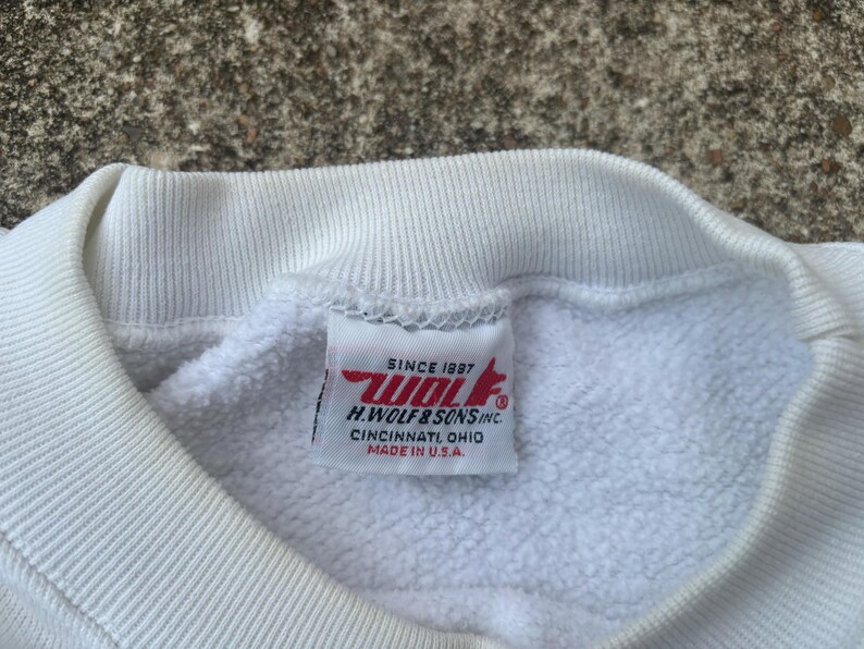 May include: White sweatshirt with a red and white label that reads "Since 1987 Wolf H. Wolf & Sons Inc. Cincinnati Ohio Made in U.S.A."