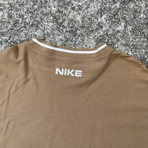May include: A brown long-sleeved shirt with a white ribbed collar and the word "NIKE" embroidered in white on the back.