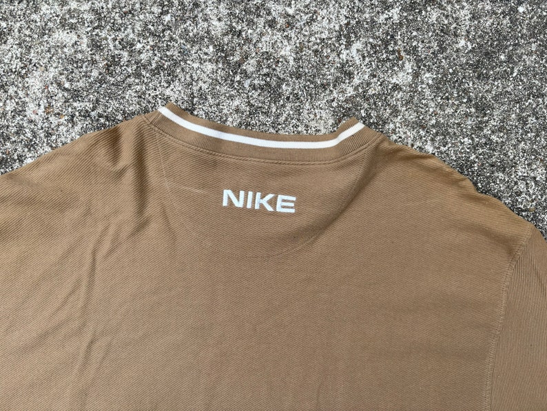 May include: A brown long-sleeved shirt with a white ribbed collar and the word "NIKE" embroidered in white on the back.