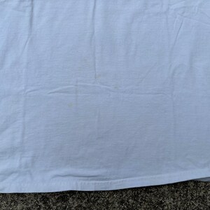 May include: A plain white t-shirt with a few small, light brown stains.