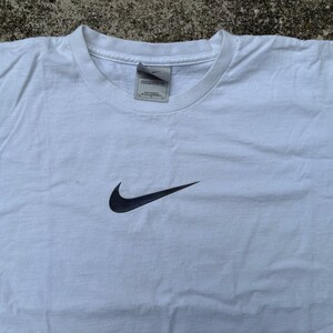 May include: White t-shirt with a black Nike swoosh logo.