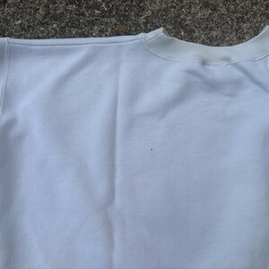 May include: White sweatshirt with a crew neck and long sleeves. The sweatshirt has a subtle striped pattern on the left sleeve.