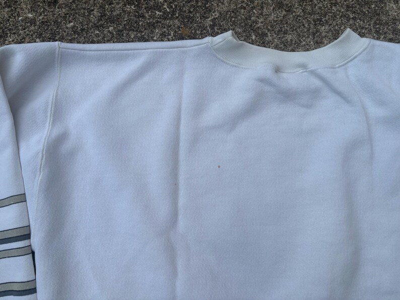 May include: White sweatshirt with a crew neck and long sleeves. The sweatshirt has a subtle striped pattern on the left sleeve.