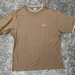 May include: A brown t-shirt with a white Nike swoosh logo. The shirt has white trim around the neckline and sleeves.