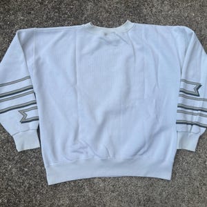 May include: White sweatshirt with black and gray striped detailing on the sleeves. The sleeves have a geometric pattern.