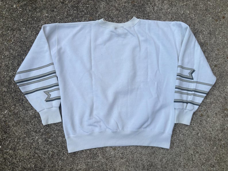 May include: White sweatshirt with black and gray striped detailing on the sleeves. The sleeves have a geometric pattern.