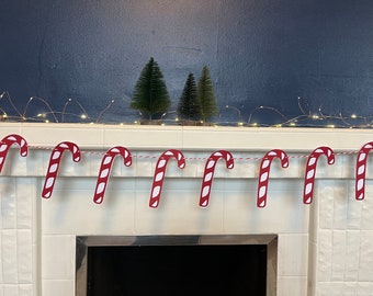 May include: A red and white candy cane garland hangs above a white tiled fireplace. The garland is strung with small white lights.