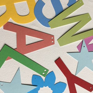 May include: A collection of colorful paper cutouts in the shape of letters, stars, and a flower. The letters are in various colors, including yellow, blue, green, red, and pink. The stars are blue and the flower is blue.