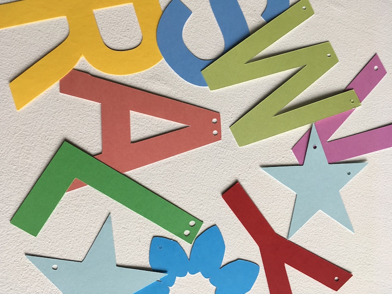 May include: A collection of colorful paper cutouts in the shape of letters, stars, and a flower. The letters are in various colors, including yellow, blue, green, red, and pink. The stars are blue and the flower is blue.