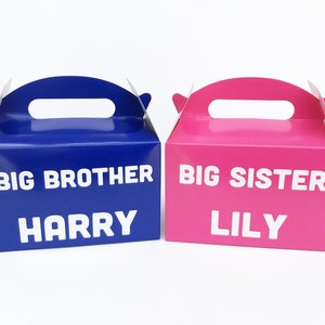 K&ouml;nnte beinhalten: Zwei Geschenkboxen, eine blaue und eine rosa, mit den Worten "Gro&szlig;er Bruder" und "Gro&szlig;e Schwester" bedruckt. Die blaue Box tr&auml;gt den Namen "Harry" und die rosa Box den Namen "Lily".