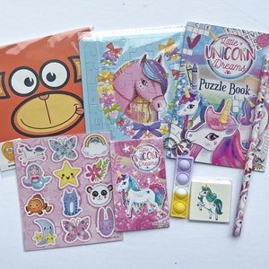 May include: A unicorn-themed activity pack for kids includes a puzzle book, stickers, a pencil, a pop-it toy, and a puzzle. The puzzle book cover features a unicorn with a rainbow mane and the words "Little Unicorn Dreams Puzzle Book".