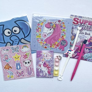 May include: A set of unicorn-themed craft supplies, including a sticker sheet with a variety of unicorn, butterfly, and star designs, a puzzle featuring a pink unicorn with a flower crown, a small book titled "Little Unicorn Dreams", a pink pen, a white unicorn charm bracelet, and a multi-colored pop-it toy.