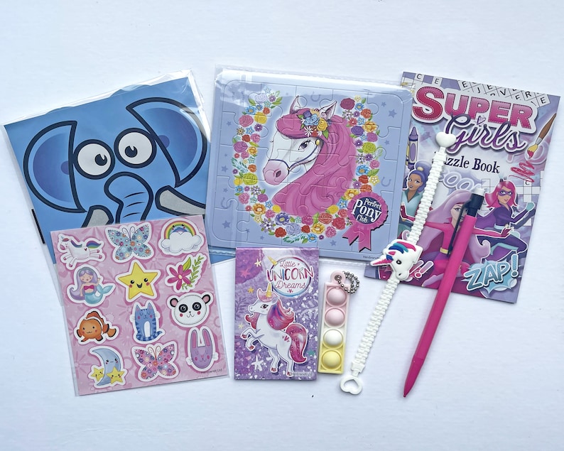 May include: A set of unicorn-themed craft supplies, including a sticker sheet with a variety of unicorn, butterfly, and star designs, a puzzle featuring a pink unicorn with a flower crown, a small book titled "Little Unicorn Dreams", a pink pen, a white unicorn charm bracelet, and a multi-colored pop-it toy.