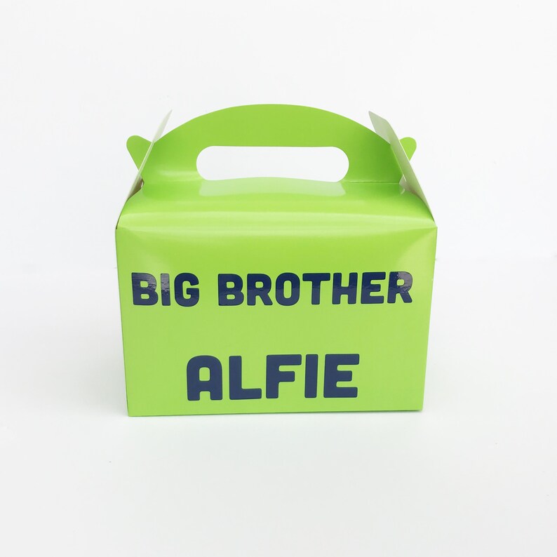 K&ouml;nnte beinhalten: Eine gr&uuml;ne Geschenkschachtel aus Pappe mit einem Griff. Auf der Vorderseite der Schachtel steht "BIG BROTHER ALFIE" gedruckt.