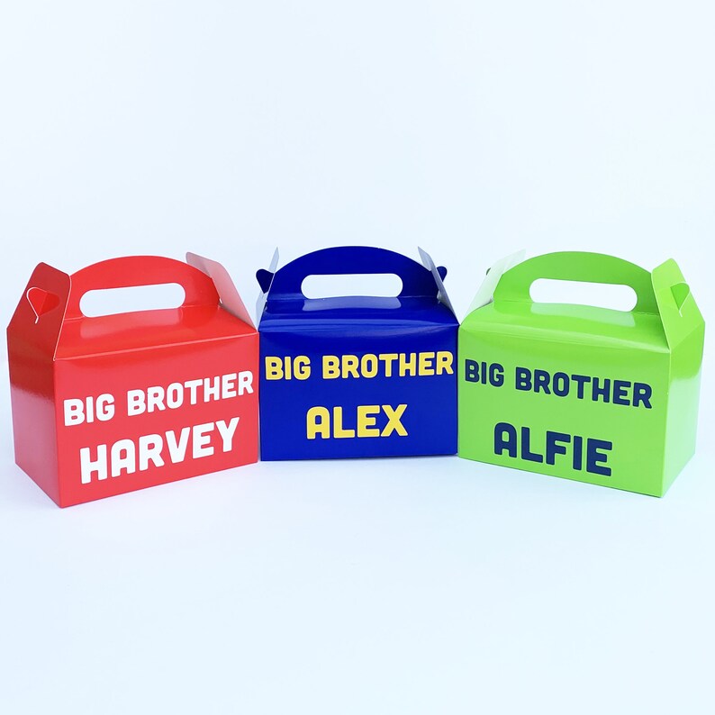 K&ouml;nnte beinhalten: Drei Geschenkboxen mit Griffen, jede in einer anderen Farbe: Rot, Blau und Gr&uuml;n. Die Boxen sind mit dem Text "Gro&szlig;er Bruder" und einem Namen verziert: Harvey, Alex und Alfie.