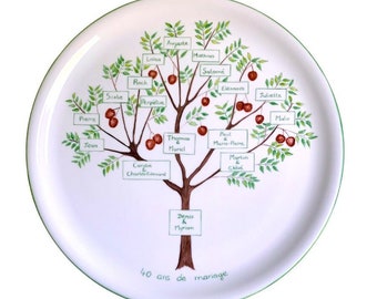 May include: A white ceramic plate with a hand-painted family tree design. The tree has green leaves and brown branches with red berries. The names of family members are written on small white rectangles attached to the branches. The text at the bottom of the plate reads "40 ans de mariage".
