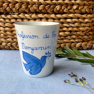 Peut inclure: Une tasse en céramique blanche avec une inscription bleue qui dit "Profession de Foi Benjamin" et une colombe bleue avec une branche d'olivier.