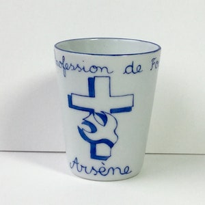 Puede incluir: Taza de cerámica blanca con borde azul y diseño azul. El diseño presenta una cruz con una paloma y el texto "Profession de Foi Arsène".