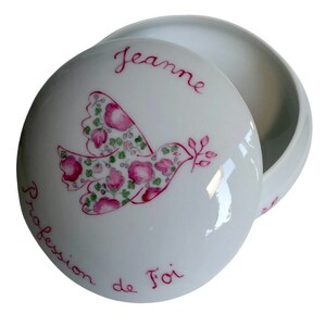 May include: A white porcelain trinket box with a lid. The lid features a dove design filled with pink flowers and green leaves, with the name "Jeanne" and the words "Profession de Foi" in red script.