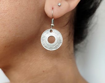 May include: Silver coin earrings with a circular design and Hebrew lettering. The earrings are hanging from a silver hook.