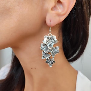 May include: Silver-toned leaf earrings. The earrings feature a cascading design of detailed leaves, each with intricate veining. The earrings are suspended from a simple hook. The jewelry is designed to be worn on the ear.