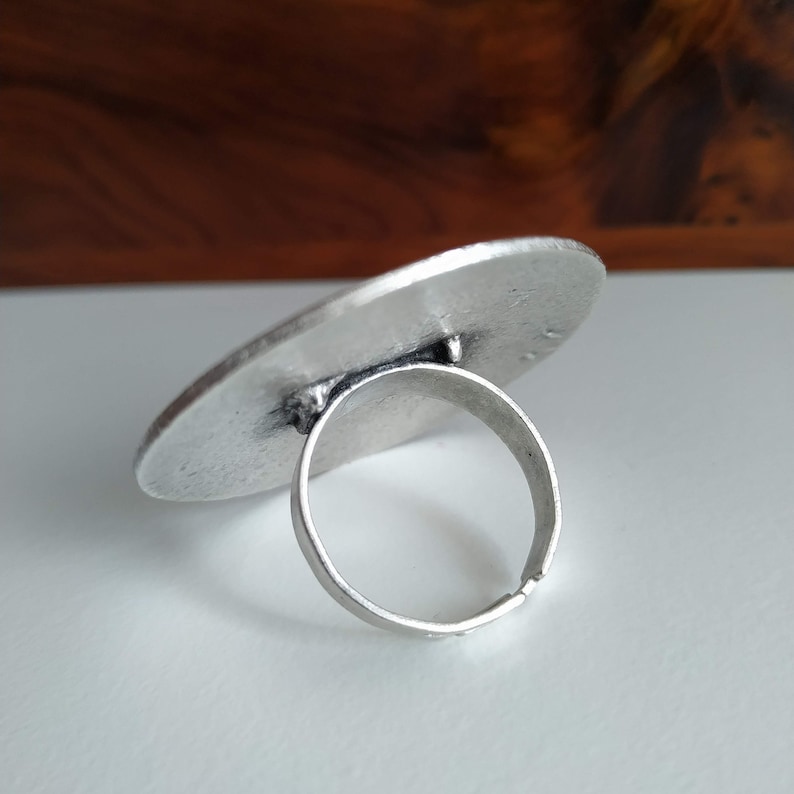 May include: A silver ring with a large, oval-shaped top. The ring is made of metal and has a simple design.