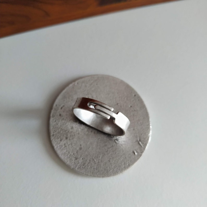 May include: A silver ring with a unique, interlocking design. The ring is displayed on a silver-colored base.