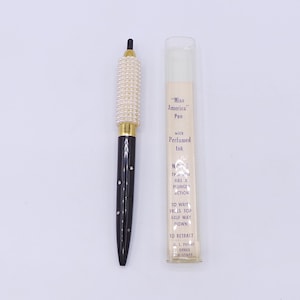 May include: A black and gold pen with a pearl-like design on the barrel. The pen is labeled "Miss America" Pen with Perfumed Ink. The label also includes instructions for using the pen.