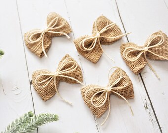 May include: Five brown burlap bows with white twine tied in the center. The bows are arranged on a white wooden surface.