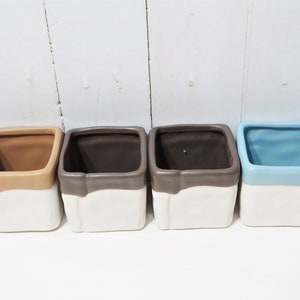 May include: Five square ceramic planters with a two-tone glaze. The planters are in shades of brown, gray, and blue. The top half of each planter is white.