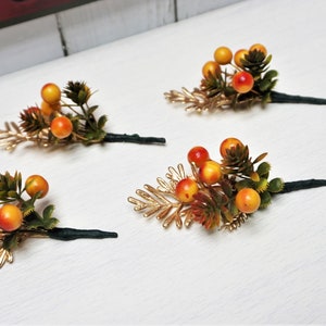 May include: Four sprigs of faux greenery with gold-toned leaves and orange berries. Each sprig has a black wire stem.