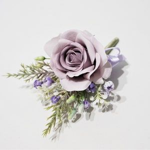 May include: A single lavender rose with small white and purple flowers and green leaves. The rose is the focal point of the arrangement.
