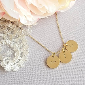 Peut inclure: Collier en or avec trois pendentifs ronds. Les pendentifs sont gravés de lettres arabes. Le collier est sur un fond blanc.