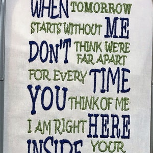 May include: Embroidered white fabric with a heartfelt message in blue and green thread. The text reads "When tomorrow starts without me, don't think we're far apart...inside your heart."