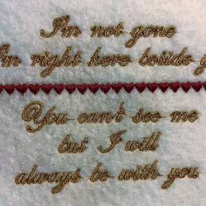 May include: Embroidered quote on a white fabric background. The quote reads "I'm not gone I'm right here beside you You can't see me but I will always be with you". A row of small red hearts separates the first two lines of text from the rest.