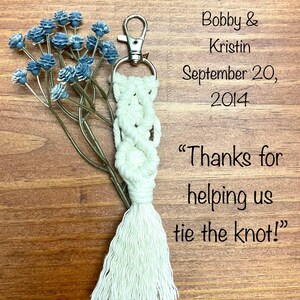 May include: White macrame keychain with a tassel, a silver key ring, and the text "Bobby & Kristin September 20, 2014 "Thanks for helping us tie the knot!"