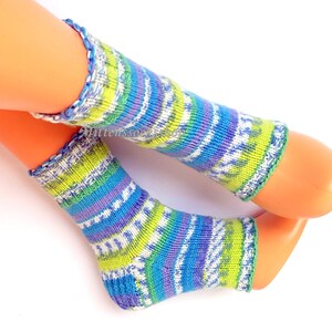 May include: A pair of colorful knitted leg warmers in shades of blue, green, purple, and white. The leg warmers have a ribbed cuff and a patterned design. The text "mittensocks.shop" is visible in the image.