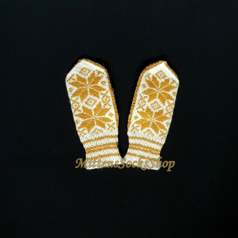May include: A pair of white knitted mittens with a gold snowflake pattern. The mittens have a ribbed cuff.