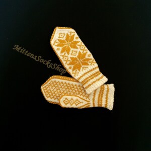 May include: A pair of knitted mittens with a white background and a yellow snowflake pattern. The mittens are folded together.
