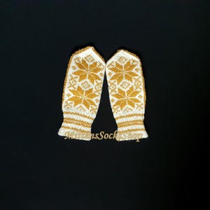 May include: A pair of white knitted mittens with a gold snowflake pattern. The mittens have a white cuff with a gold stripe.