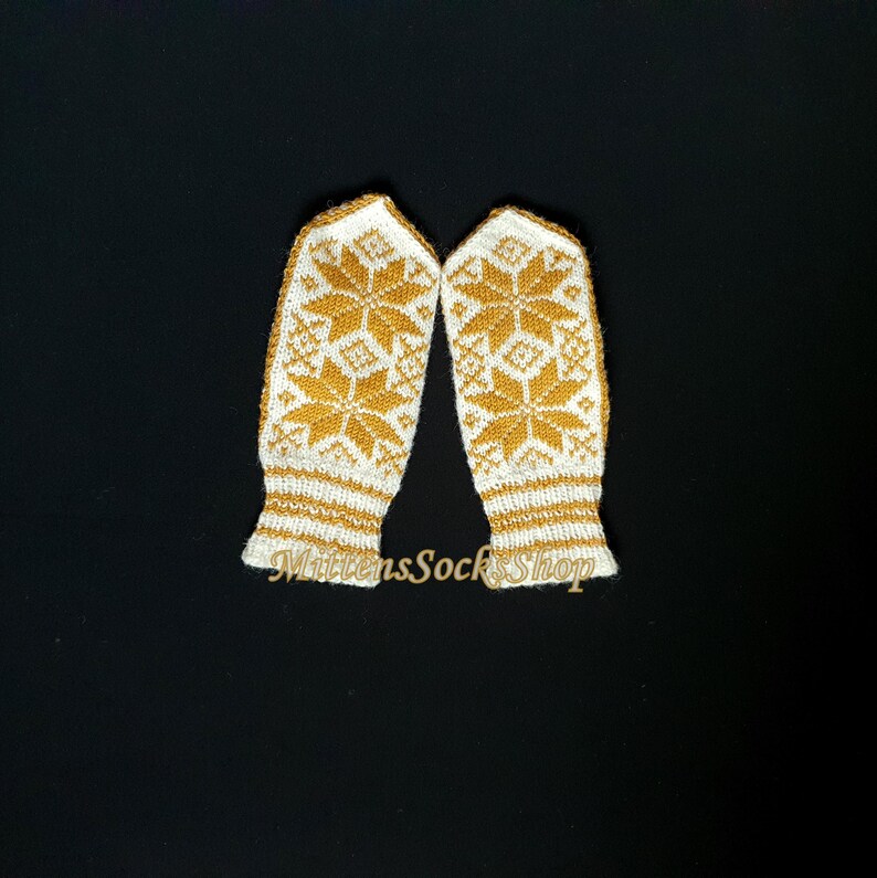May include: A pair of white knitted mittens with a gold snowflake pattern. The mittens have a white cuff with a gold stripe.