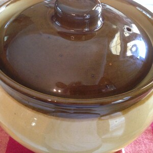 May include: A brown and beige ceramic pot with a lid. The pot has a smooth, glossy finish and a rounded shape. The lid has a small hole in the center.