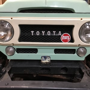 Op de afbeelding: Een lichtgroene Toyota Land Cruiser met een wit en zwart grille. Het Toyota-logo is zichtbaar aan de voorkant van het voertuig.