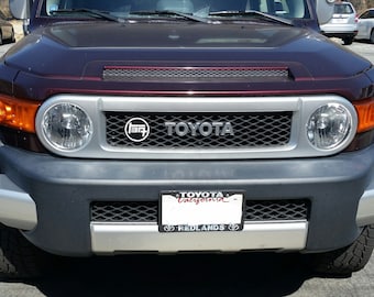 Puede incluir: Un Toyota FJ Cruiser rojo oscuro con una parrilla negra y un parachoques plateado. El coche tiene una matrícula negra que dice "TOYOTA California" y "REDLANDS".