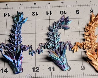 May include: Three small, detailed dragon figurines. The dragons are made of a shiny, iridescent material that appears to be blue, green, and purple. The dragons are posed in a standing position with their tails curled up. The dragons are on a white grid background.