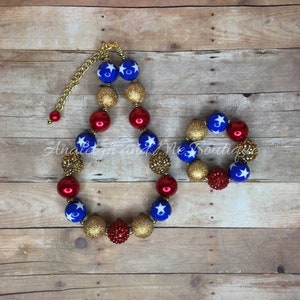 Pu&ograve; includere: Un set di collana e braccialetto con perline rosse, bianche e dorate con stelle. La collana ha una chiusura a catena dorata.