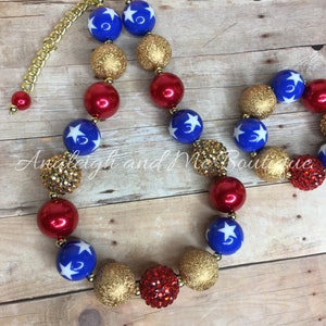 Pu&ograve; includere: Una collana di perline rosse, dorate e blu con stelle bianche. La collana ha una chiusura a catena dorata.