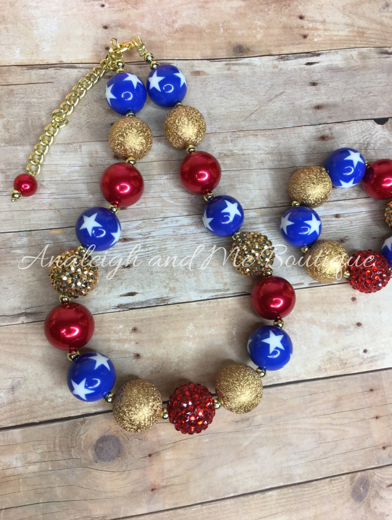 Pu&ograve; includere: Una collana di perline rosse, dorate e blu con stelle bianche. La collana ha una chiusura a catena dorata.