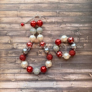 May include: Red, white, and silver chunky bead necklace and bracelet set with snowflake accents. The necklace has a silver chain clasp.