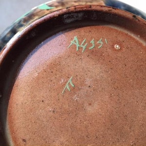 May include: Close-up of the bottom of a brown ceramic bowl with a green glaze. The bowl has a blue and brown design on the outside. The bottom is marked with the text "A4351" and a green "T".